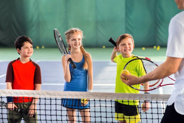 Excited children are listening to explanations of their tennis trainer with attention. They are holding rackets and laughing. Portrait